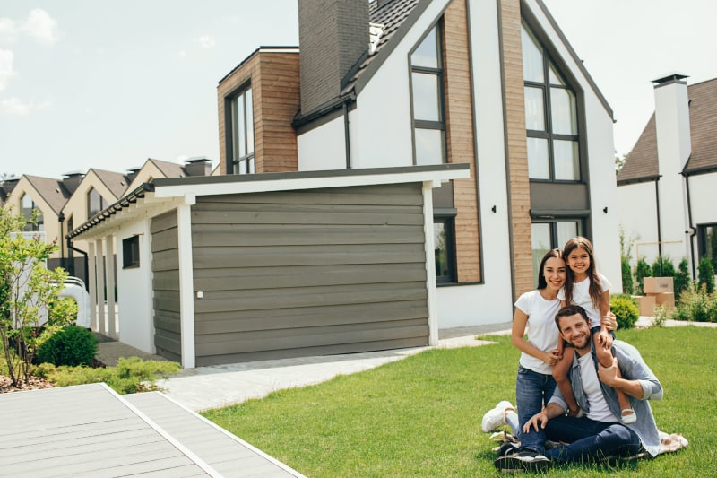 family sitting on grass in front of house smiling at camera