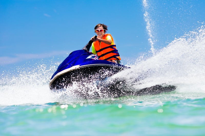 young man in orange life jacket on blue jetski in the ocean